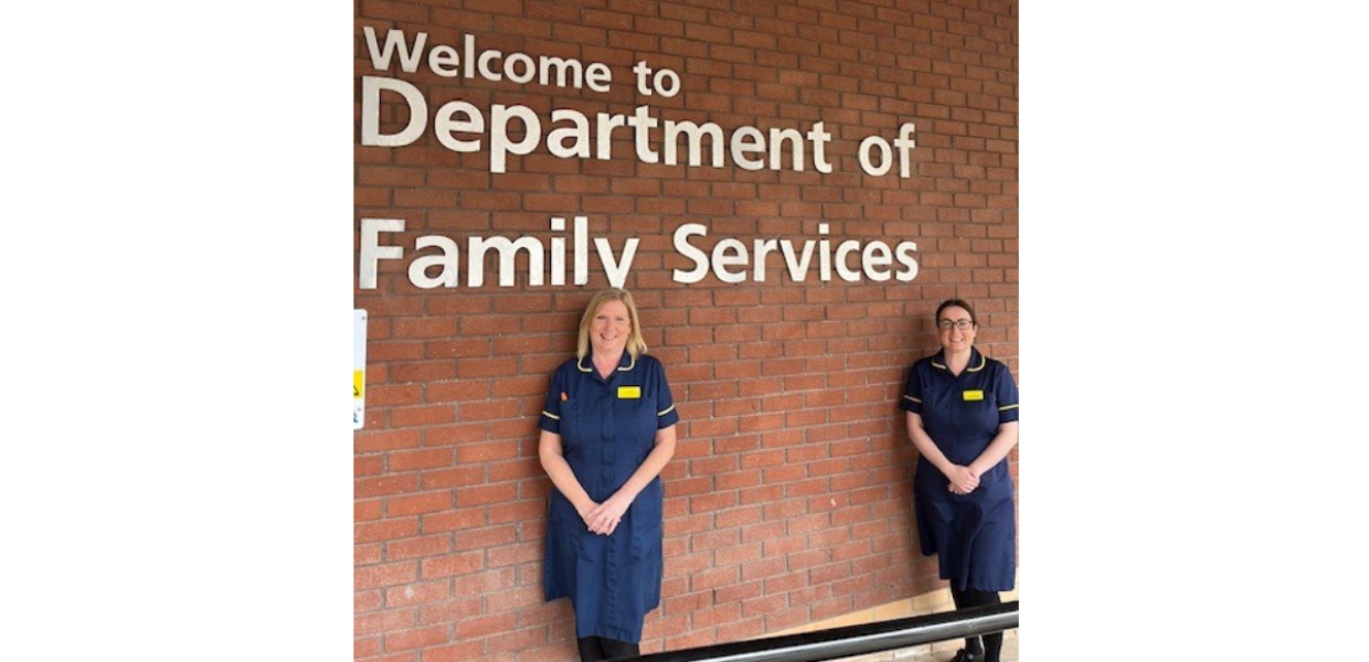 Two nurses in a blue uniform are standing against a wall which says Department of Family Services